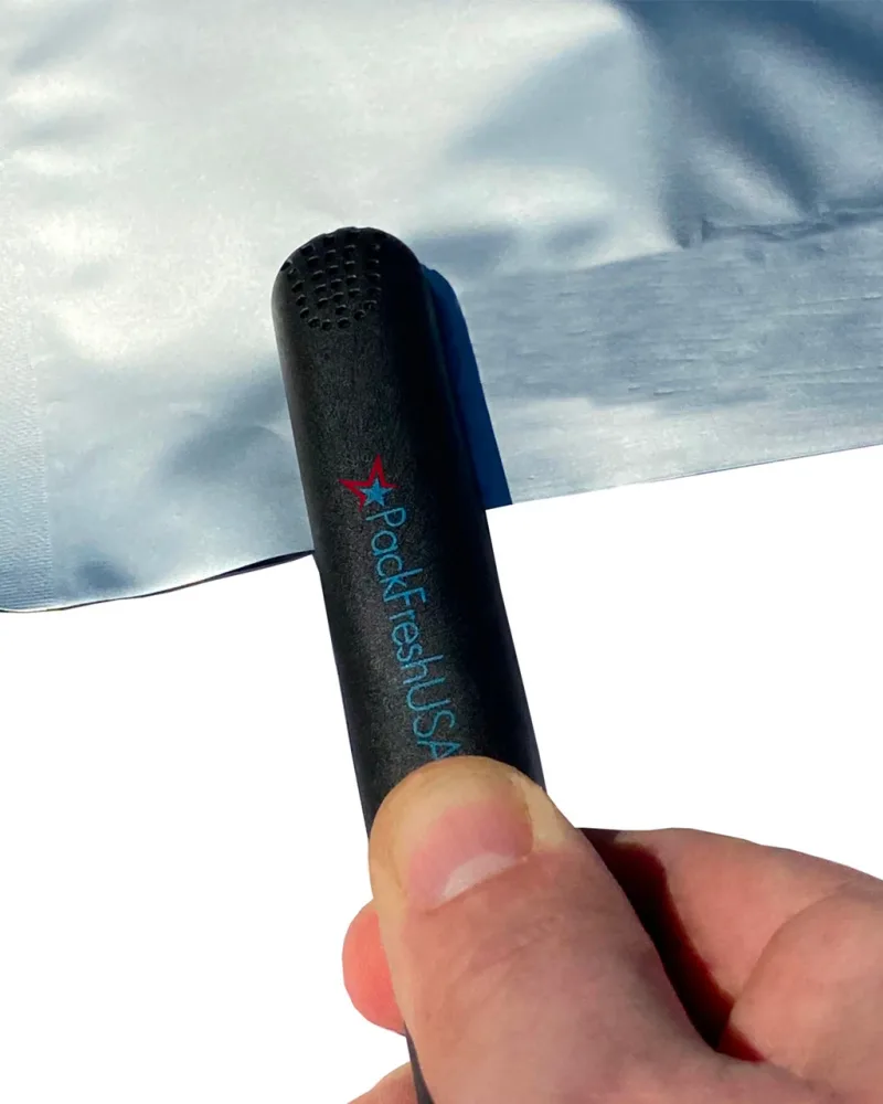 A hand closing a PackFreshUSA mini bag sealer across the open top of a Mylar bag.